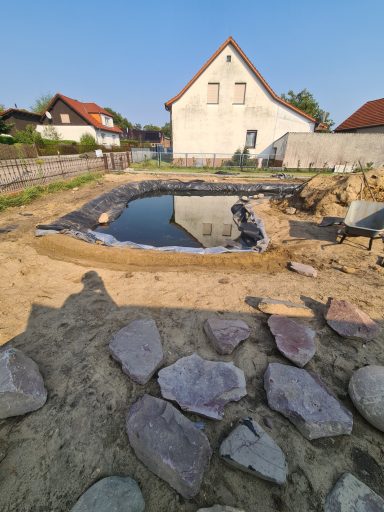 Bauplatz mit gegrabenem Teich, Steinen und einem Haus im Hintergrund.