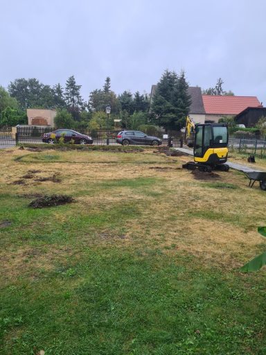Baustelle mit Bagger auf unebenem, frisch bearbeitetem Erdreich unter bewölktem Himmel.