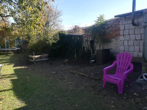 Ein Gartenbereich mit einem lila Stuhl und Blick auf Bäume und eine Mauer.